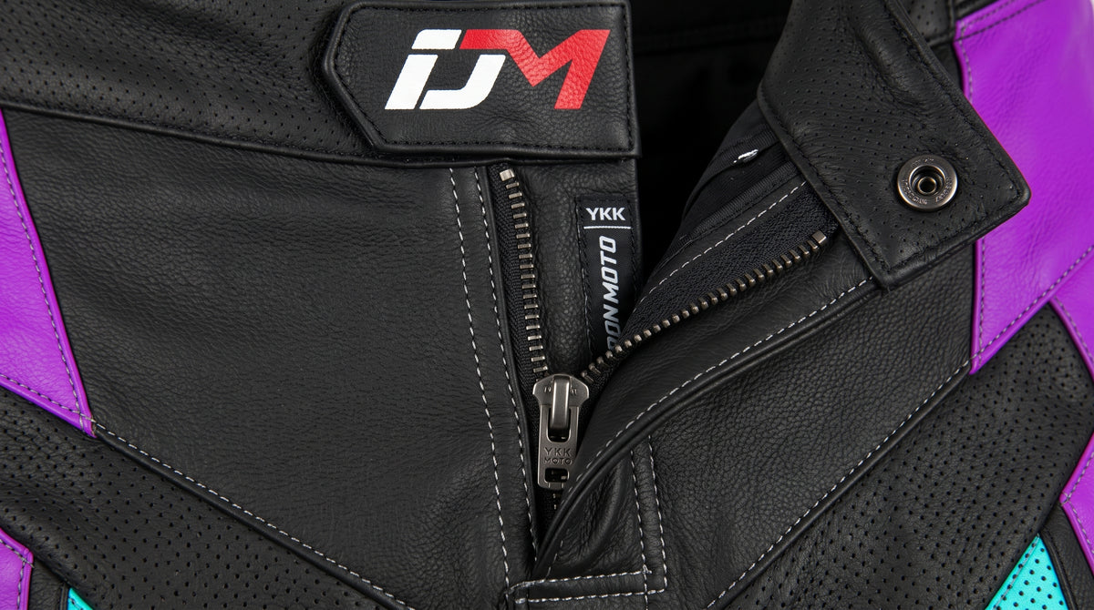 Close-up of a black leather motorcycle jacket with purple side panels, a black zipper, and a visible IDM logo patch on the chest.