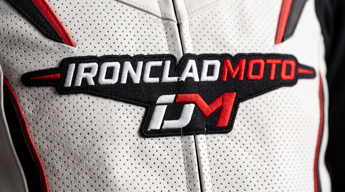 Close-up of a white perforated leather motorcycle jacket with a black, white, and red embroidered 'IRONCLAD MOTO' patch on the chest.