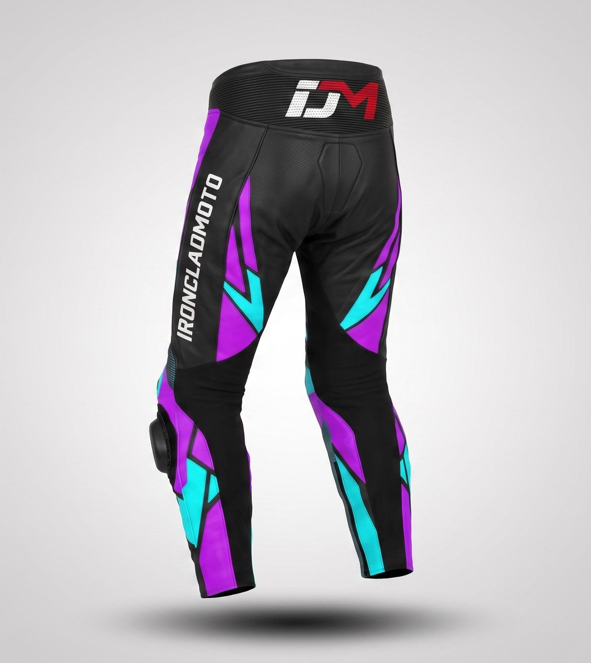 Black motorcycle pants with purple and teal geometric graphics, featuring a white and red IDM logo on the waistband and 'IRONCLADMOTO' printed down the left leg, shown on a light gray background.
