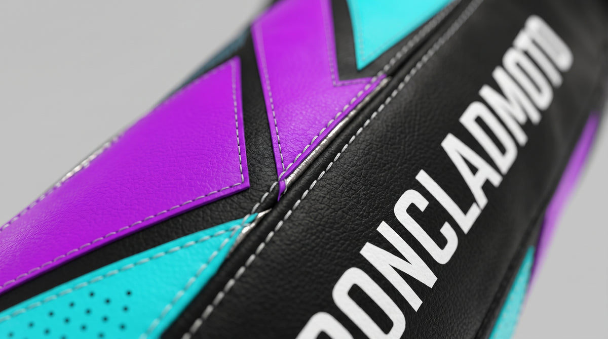 Close-up of a motorcycle leather cover with black, purple, and turquoise panels, featuring the white 'PONCLADMOTO' brand name on the side.