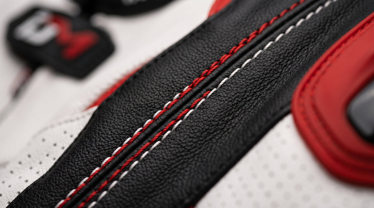 Close-up detail of a sneaker showing black textured leather, white perforated panels, red stitching, and red trim.